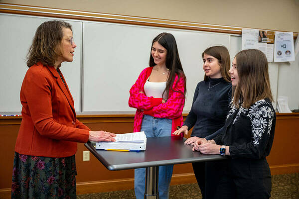 Three students from Ukrainian Catholic University speak with a faculty member in a classroom.