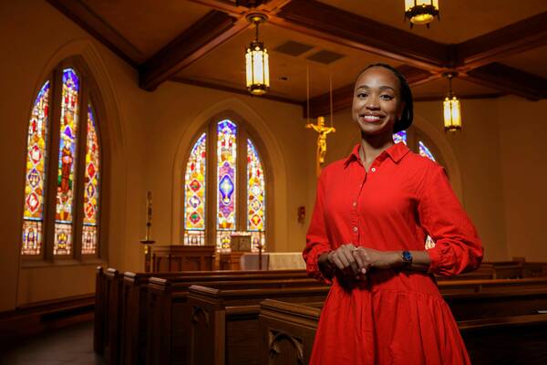 A woman in a red dress smiles inside a church with stained-glass windows.