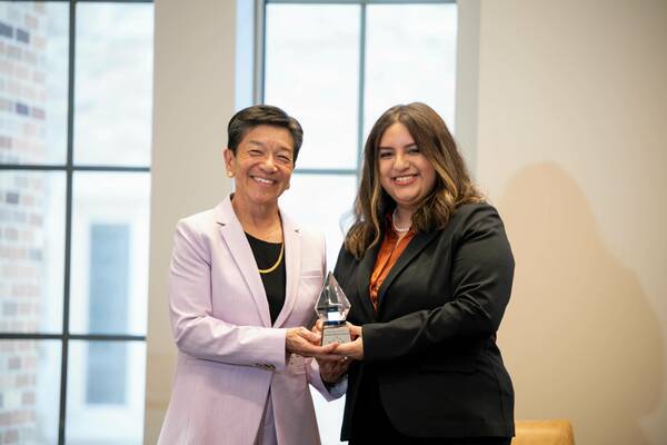 A woman with short dark hair in a purple blazer and a woman with long brown hair in a black blazer smile while holding a crystal award. The award features "Notre Dame Law School" and "Olivarez Award."