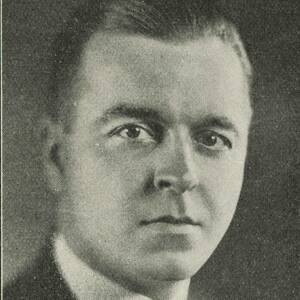 Black and white portrait of a man with short dark hair, wearing a suit and tie, looking forward with a serious expression.