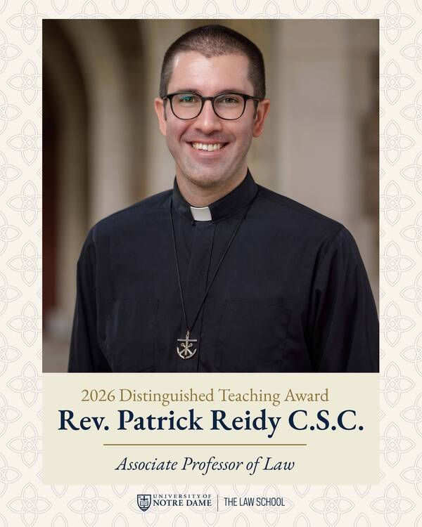 Rev. Patrick Reidy C.S.C. smiles, wearing black clerical attire, glasses, and an anchor-cross pendant.