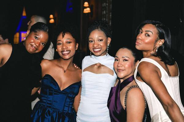 Five women in black, blue, white, and purple dresses smile at an evening event.