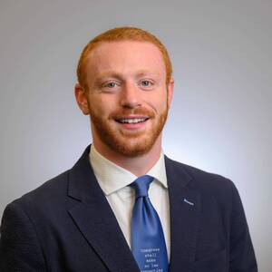 Smiling man with red hair and beard in navy suit. Blue tie features text: Congress shall make no law respecting.(Sam Foer)
