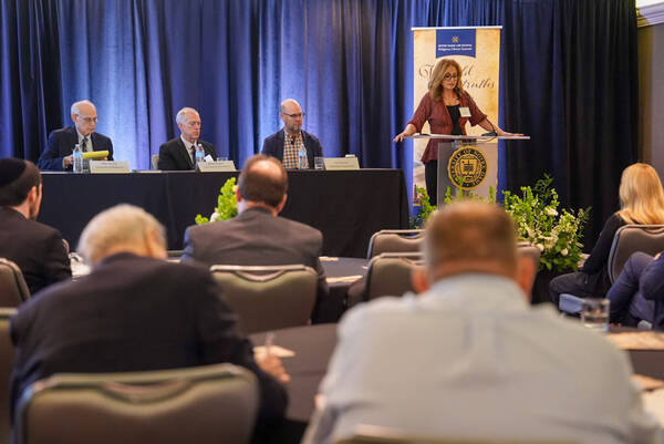 Woman speaks at Notre Dame Law School Religious Liberty Summit podium. Panelists Alton Hertzler, Daniel Philpott, Rick Garnett listen.