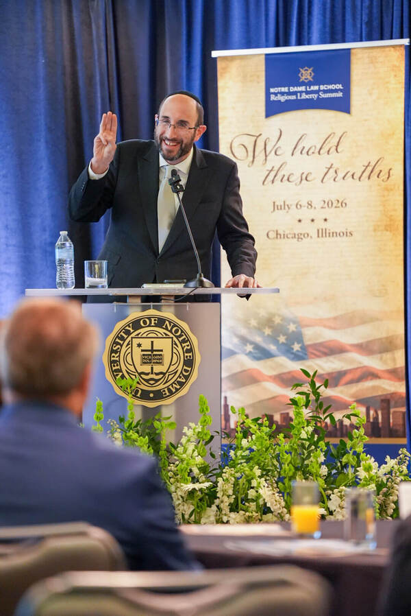 Smiling man in yarmulke and suit speaks at a Notre Dame podium, gesturing with three fingers. A "Religious Liberty Summit" banner is behind him. (Rabbi Meir Soloveichik)