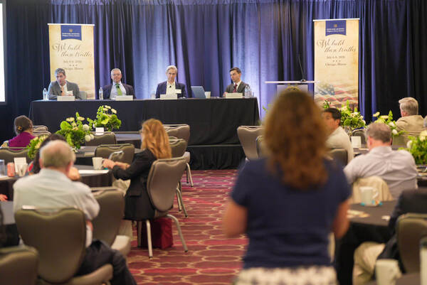 Four men on stage at the Notre Dame Law School Religious Liberty Summit, with audience and "We hold these truths" banner.
