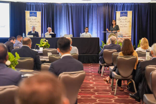 Woman speaks at a podium during the Notre Dame Law School Religious Liberty Summit in Chicago. Panelists and audience present.