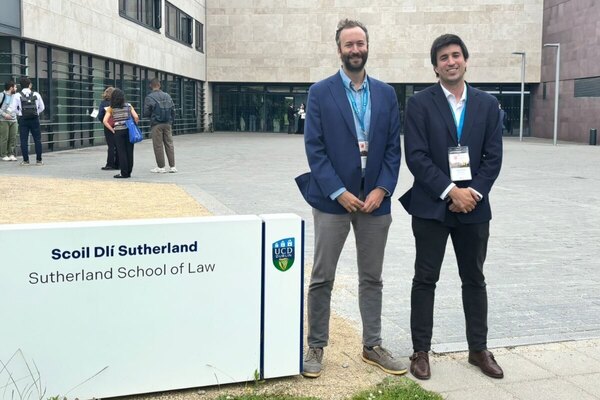 Two smiling men in dark blazers stand beside a Sutherland School of Law sign, UCD Dublin, outside a modern building.