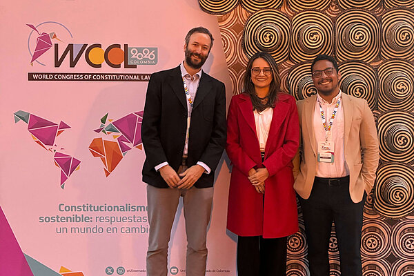 Three people smile at WCCL 2026 Colombia. The background shows the event logo, a geometric map, and a wall of Colombian hats.