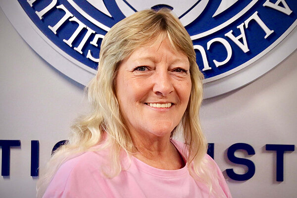 Smiling woman with blonde hair in pink shirt. Behind her, blue and white raised letters at Notre Dame.