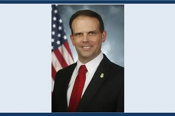 Man in black suit and red tie smiles next to an American flag. (James McCament ‘20 J.D.)