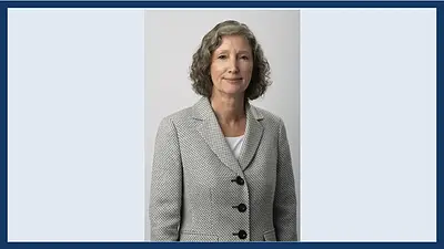 Woman with curly gray hair smiles, wearing a patterned gray jacket over a white shirt. (Lynn McGuire ‘97 J.D.)