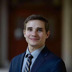 A young man in a navy suit and striped tie smiles warmly. (Steven Henderson)