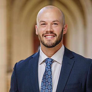 Bald man in a suit and blue patterned tie smiles, with Notre Dame's Bond Hall archway in the background. (Zachary Boeckmann)