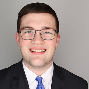 Man in a suit and tie smiles, wearing glasses. (Josh Arsulowicz)