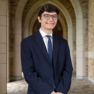 Young man in dark suit and patterned tie smiles in front of Notre Dame arches. (Nicolas Bianco)